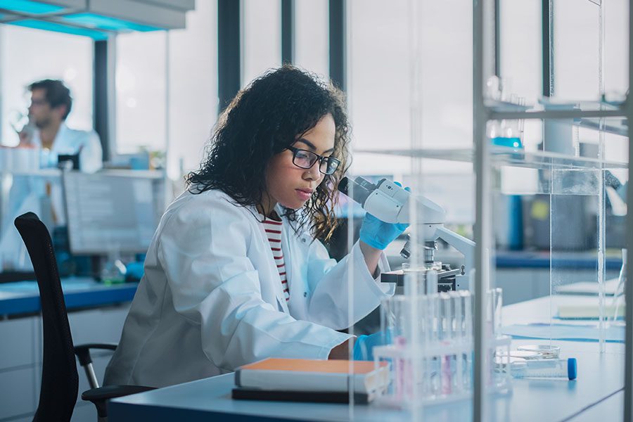 Biotechnology Business Insurance - Young Biotechnology Specialist Using a Microscope and Doing Analysis of a Test Sample While Working with Advanced Equipment Medical in a Laboratory