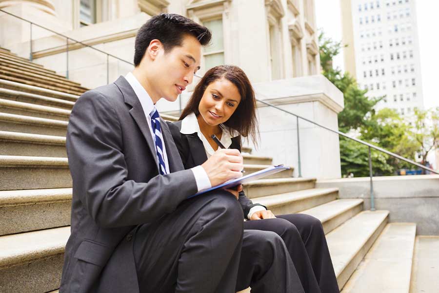 Business Insurance - Two Business Colleagues Sitting On Municiple Steps and Working Together Outdoors
